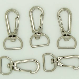 Peut inclure: Cinq fermoirs pivotants argentés avec un fermoir à ressort. Ces fermoirs sont couramment utilisés pour attacher des sangles, des laisses ou d'autres accessoires.
