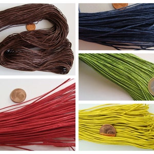 Op de afbeelding: Een verzameling gekleurde koorden in bruin, marineblauw, groen, rood en geel. Elke kleur is apart gebundeld, met een munt naast elke bundel als referentie voor de grootte. Deze koorden worden waarschijnlijk gebruikt voor knutselen of het maken van sieraden.