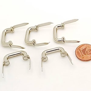 Peut inclure: Cinq poignées en métal argenté avec des extrémités pointues. Les poignées sont en forme de rectangle aux coins arrondis. Une pièce d'un euro est incluse pour l'échelle.