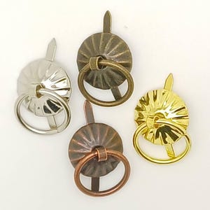 Può includere: Quattro pomelli per cassetti in metallo con finiture argento, bronzo antico, rame e oro. Ogni pomello presenta una piastra circolare scanalata con un anello centrale e una punta metallica che sporge dalla parte superiore per il fissaggio.