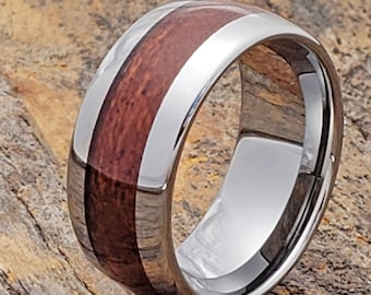 May include: A silver tungsten carbide ring with a brown wood inlay. The ring is polished and has a beveled edge.