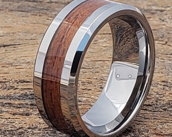 May include: A silver tungsten carbide ring with a brown wood inlay. The ring has a bevelled edge and a polished finish.