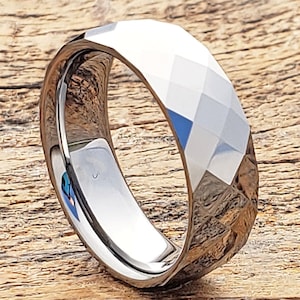May include: A silver tungsten carbide ring with a faceted, diamond-cut design. The ring is polished and has a smooth, shiny finish.