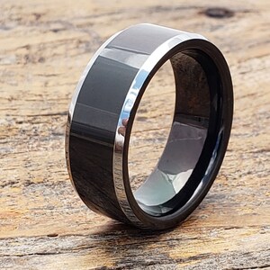 May include: A black tungsten carbide ring with a silver beveled edge. The ring is polished and has a high shine.