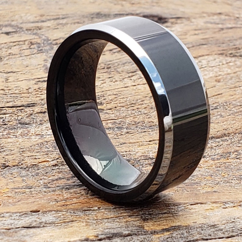 May include: A black and silver beveled edge tungsten carbide ring.