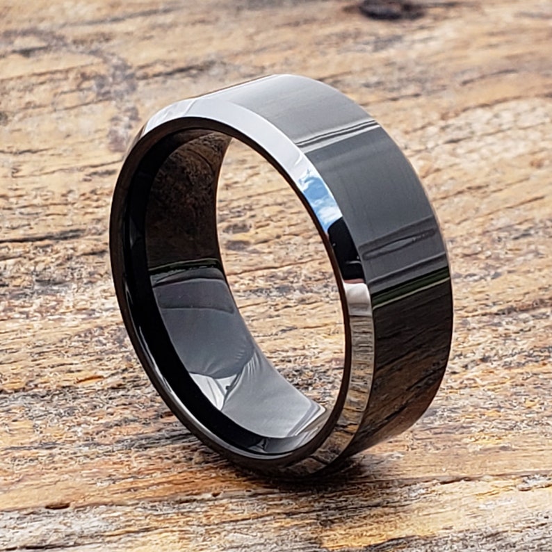 May include: A black tungsten carbide ring with a beveled edge. The ring is polished and has a shiny finish.