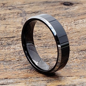 May include: A black tungsten carbide ring with a beveled edge. The ring has a polished finish and a subtle shine.