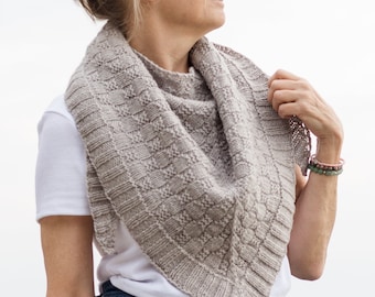 May include: A woman wearing a light gray knitted shawl with a white t-shirt and blue jeans.