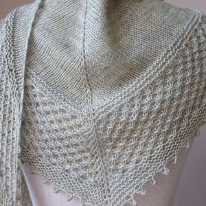 May include: A light green knitted shawl with a lacy pattern and a long fringe. The shawl is draped over a white mannequin.