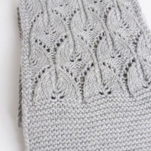 May include: Gray knitted scarf with a cable knit pattern and a delicate lace design.