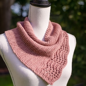 Peut inclure: Une écharpe en tricot rose poussiéreux avec un motif de dentelle délicat. L'écharpe est drapé autour d'un mannequin blanc.