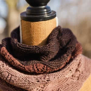 May include: A brown, pink, and black knitted scarf on a wooden mannequin.