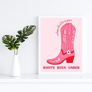 May include: A framed art print with a pink cowboy boot illustration and the red text "whose bed have your BOOTS BEEN UNDER". The boot design includes floral and scroll details.