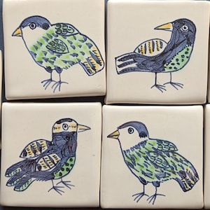 May include: A set of six square ceramic tiles featuring hand-drawn illustrations of birds. Each tile displays a unique bird in shades of blue, green, and yellow against a cream-coloured background. The birds are depicted in various poses.