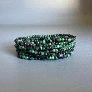 May include: A stack of green, black, and pink gemstone bracelets. The bracelets are made of small, round beads.