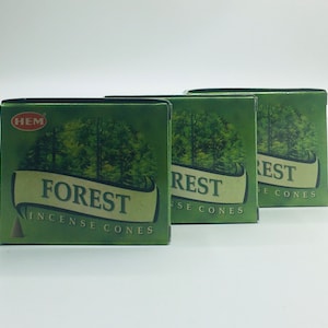 以下が含まれることがあります： 「FOREST」のお香コーンの緑色の箱が3つ。各箱には森の風景と「FOREST INCENSE CONES」の文字が描かれています。箱は白い背景に並んでいます。「HEM」のブランドが箱の左上に表示されています。