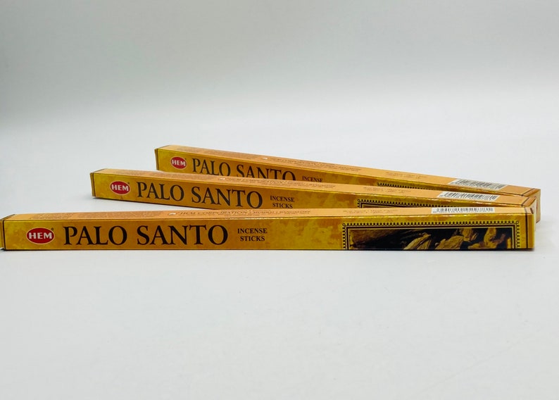 May include: Three rectangular boxes of Palo Santo incense sticks. The boxes are primarily gold with brown text and a decorative border. The text on the boxes reads "PALO SANTO INCENSE STICKS". The brand name "HEM" is also visible.
