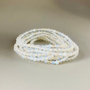 May include: A stack of white opal bead bracelets. The beads are small and round, and the bracelets are layered on top of each other.