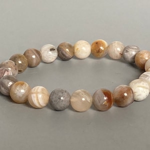 May include: A bracelet made of light brown, white, and gray agate beads. The beads are round and have a natural, polished finish.