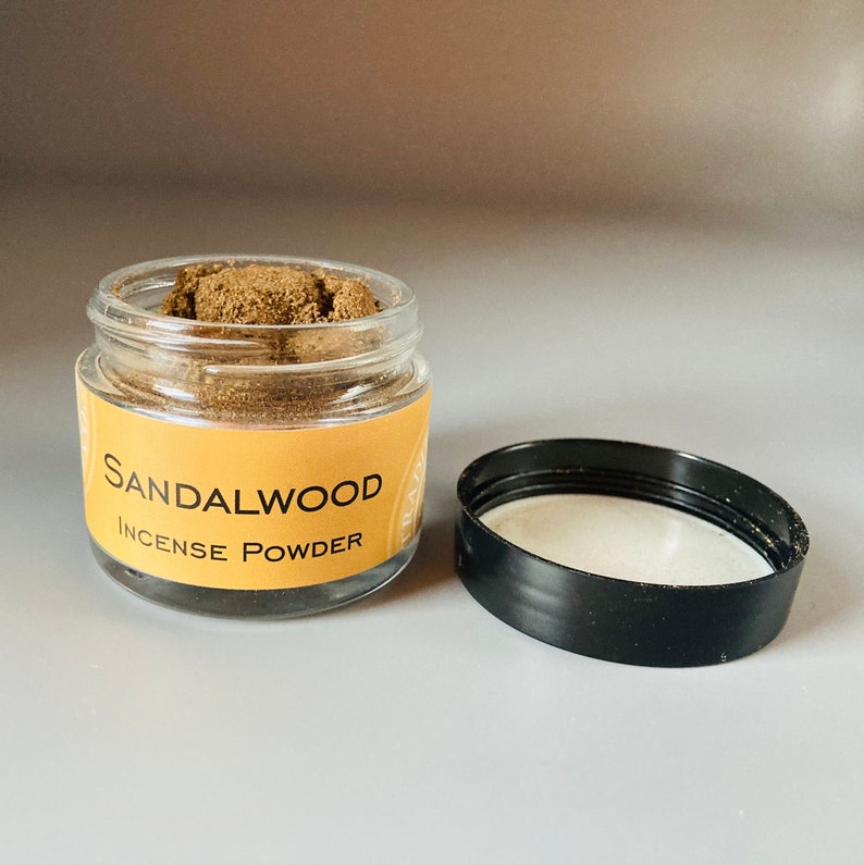 May include: A glass jar with a black lid filled with brown sandalwood incense powder. The label on the jar reads "Sandalwood Incense Powder".