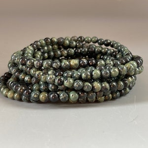 May include: A strand of dark green and black beads, with a speckled pattern, is coiled into a circle.