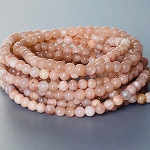 Op de afbeelding: Een stapel sunstone kralen armbanden in een licht perzikkleurige kleur. De kralen zijn rond en glad.