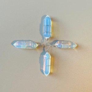 May include: Four iridescent opal point pendants wrapped in silver wire. The pendants are arranged in a cross shape on a light grey background.