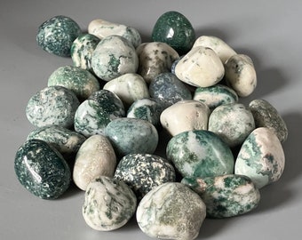 May include: A collection of green and white moss agate tumbled stones. The stones are smooth and polished, with a variety of patterns and colors.