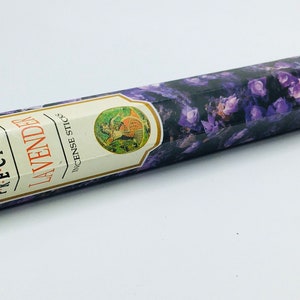 Puede incluir: Una caja de inciensos Hem Precious Lavender en forma de varillas, de color morado y blanco. La caja presenta un diseño floral y el texto "HEM PRECIOUS LAVENDER INCENSE STICKS".