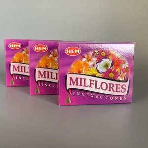 May include: Three boxes of "Milflores Incense Cones" are displayed. The boxes are a vibrant purple with a floral design and the brand "HEM" in a red circle. The boxes are arranged in a row, with the front box in focus.