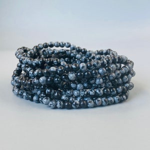 May include: A stack of black and white speckled stone bracelets. The bracelets are made of small, round beads.