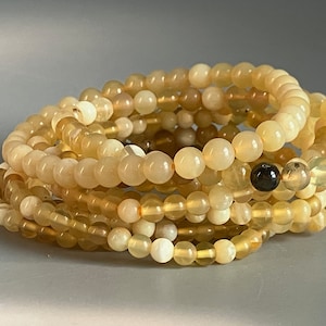 May include: A stack of yellow opal beaded bracelets. The bracelets are made with round, smooth beads and have a subtle iridescent sheen.