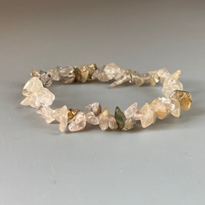 Puede incluir: Un brazalete de chips de cristal de cuarzo transparente con inclusiones doradas y marrones. El brazalete está hecho de pequeños chips de cuarzo de forma irregular.