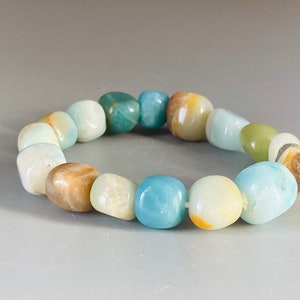 Puede incluir: Un brazalete hecho de piedras lisas, redondeadas y multicolores. Las piedras son de tonos azules, verdes y marrones.