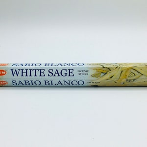 May include: A box of HEM White Sage incense sticks. The box is white with blue text and a picture of sage leaves. The text on the box reads "SABIÓ BLANCO WHITE SAGE INCENSE STICKS SABIÓ BLANCO INCIENSO"