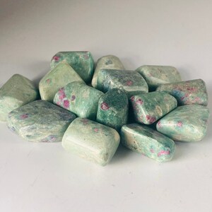 May include: A collection of tumbled green and pink ruby zoisite stones. The stones are smooth and polished, with a variety of shapes and sizes.