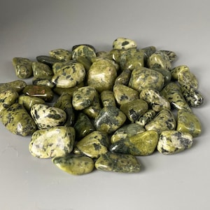 May include: A pile of green and black speckled tumbled stones. The stones are smooth and polished.