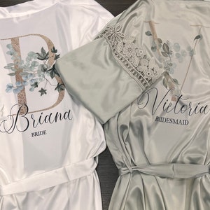 Peut inclure: Deux robes en satin blanc avec des motifs floraux et des bordures en dentelle. La robe de gauche indique "Briana Bride" et la robe de droite indique "Victoria Bridesmaid".