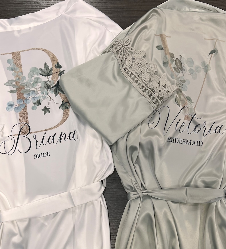Peut inclure: Deux robes en satin blanc avec des motifs floraux et des bordures en dentelle. La robe de gauche indique "Briana Bride" et la robe de droite indique "Victoria Bridesmaid".