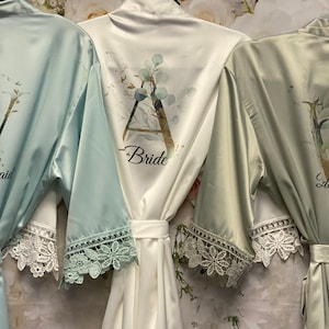 Peut inclure: Trois robes en satin avec bordure en dentelle. Les robes sont dans des tons de vert et de blanc. Les robes sont personnalis&eacute;es avec les mots "Bride", "Bridesmaid" et "Bridesmaid".
