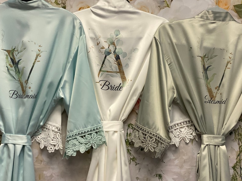 Peut inclure: Trois robes en satin avec bordure en dentelle. Les robes sont dans des tons de vert et de blanc. Les robes sont personnalis&eacute;es avec les mots "Bride", "Bridesmaid" et "Bridesmaid".