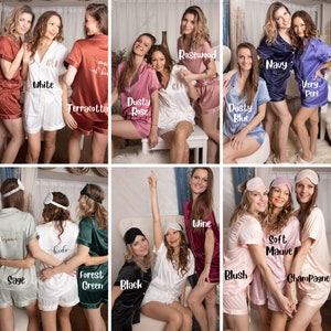 May include: A collection of women's satin pajama sets in various colors, including white, terracotta, dusty rose, navy, and forest green. Each set includes a short-sleeved top and shorts. Some sets have text on them.