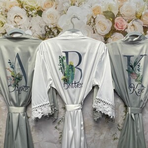 Peut inclure: Trois robes en satin avec bordure en dentelle et broderie personnalis&eacute;e. Les robes sont en vert sauge et blanc avec des motifs floraux et les lettres A, B et K. Les noms "Ande", "Brittnee" et "Kae" sont brod&eacute;s sur les robes.