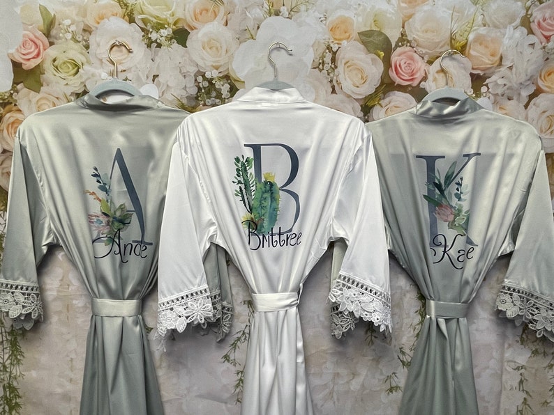 Peut inclure: Trois robes en satin avec bordure en dentelle et broderie personnalis&eacute;e. Les robes sont en vert sauge et blanc avec des motifs floraux et les lettres A, B et K. Les noms "Ande", "Brittnee" et "Kae" sont brod&eacute;s sur les robes.