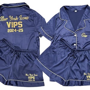 May include: Navy blue satin pajama set with white piping. The set includes a button-down shirt and shorts. The shirt features the text "New York Icons VIPS 2024-25" on the back and "Gia" on the front.