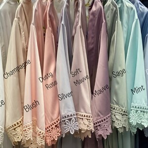Peut inclure: Dix robes en satin de diff&eacute;rentes couleurs, dont blanc, champagne, blush, rose poudr&eacute;, argent, mauve doux, mauve, sauge, menthe et bleu poussi&eacute;reux. Chaque robe est orn&eacute;e d'une bordure en dentelle et est suspendue &agrave; un cintre.