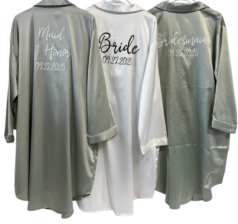 Puede incluir: Tres batas de sat&eacute;n en diferentes colores, con las palabras "Maid of Honor", "Bride" y "Bridesmaid" y las fechas impresas en la parte posterior.