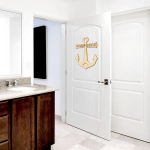 K&ouml;nnte beinhalten: Ein Anker aus Holz mit dem Text "POOP DECK" ist an einer wei&szlig;en T&uuml;r in einem Badezimmer angebracht. Der Anker ist hellbraun.