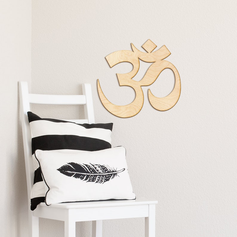 May include: A white chair with black and white striped pillows and a white pillow with a black feather design. A wooden Om symbol is mounted on the wall behind the chair.