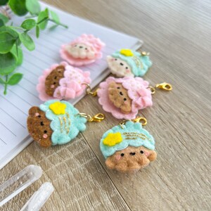 Peut inclure: Six breloques en feutre de différentes couleurs et motifs. Les breloques représentent un nuage, une étoile et un ours avec un visage mignon. Les breloques sont attachées à des porte-clés dorés.